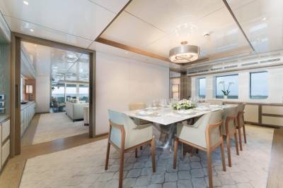 A modern dining room on a yacht is set for a formal meal with a view of the ocean.