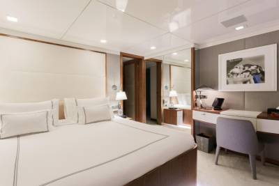 A luxurious bedroom features a large bed, a desk with a tablet, and a framed photograph above a textured wall.