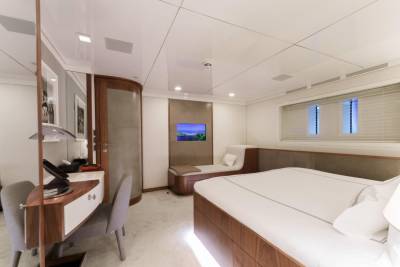 This luxurious yacht cabin features a spacious bed, a comfortable chaise lounge, and a modern desk with a view of the ocean.