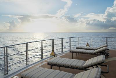 A serene ocean view with a deck featuring comfortable lounge chairs, overlooking the tranquil waters and a dramatic sky with billowing clouds.
