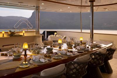 A lavishly set dining table with an array of dishes, glassware, and candles, overlooking a scenic lake and mountainous landscape through large windows.