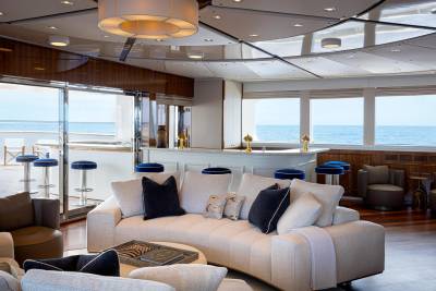 A luxurious and spacious living room with large windows offering a panoramic view of the ocean, featuring plush white sofas, decorative pillows, and a modern lighting fixture overhead.