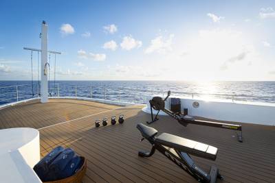 A wooden deck on a cruise ship overlooking the vast, serene ocean under a clear blue sky with fluffy white clouds.