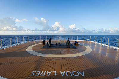 A wooden deck with a circular pattern on a cruise ship, overlooking the vast expanse of the open ocean and a cloudy sky.