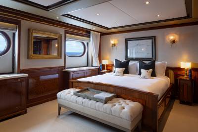 A luxurious and well-appointed bedroom with wooden paneling, large windows, and elegant furnishings, including a plush tufted bench at the foot of the bed.