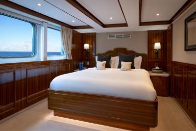 A luxurious bedroom with a large bed, wooden paneling, and a scenic ocean view through the window.