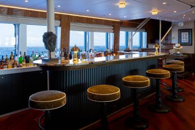A well-appointed bar with a wooden counter, stools, and a panoramic view of a cityscape through large windows.