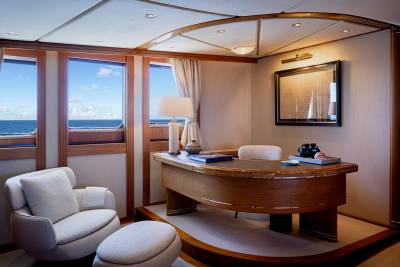 A luxurious cabin on a cruise ship, with a wooden desk, plush chairs, and a panoramic view of the ocean through large windows.