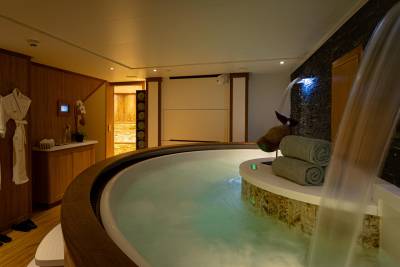 A luxurious spa-like bathroom with a large circular bathtub filled with water, surrounded by wooden and stone elements, creating a serene and relaxing atmosphere.