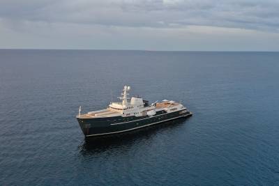 A large, black and white ship is sailing on a calm, gray ocean under an overcast sky.