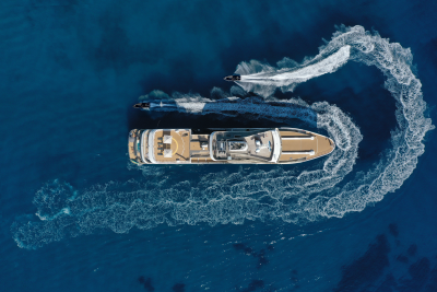 A large yacht is seen speeding across the deep blue ocean, leaving a trail of white, foaming wake behind it.