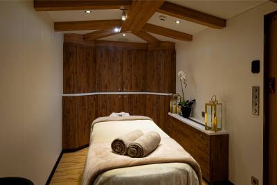 A cozy and inviting massage room with wooden beams, a massage table with towels, and various decorative elements such as candles and an orchid.