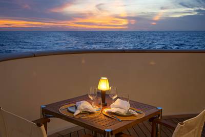 A cozy outdoor dining setup with a glowing lamp and a scenic sunset view over the ocean.