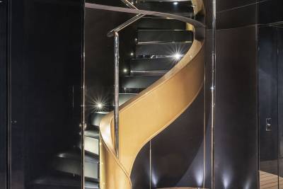 A spiral staircase with a curved wooden handrail and illuminated steps stands in a dark, sleek interior space.