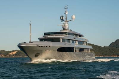A large, luxurious yacht navigates the open waters, surrounded by a picturesque coastal landscape in the background.