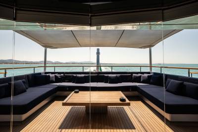 A modern, glass-enclosed lounge area with comfortable seating and a wooden table, overlooking a scenic coastal landscape.