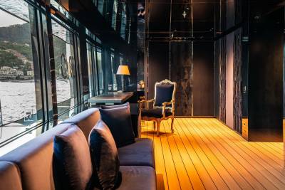 A cozy and inviting interior space with large windows overlooking a scenic body of water, featuring plush seating, warm lighting, and a wooden floor.
