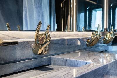 A row of golden faucet handles on a marble countertop, with a mirrored background reflecting the scene.
