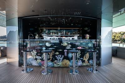 A modern and stylish bar with a glass-enclosed aquarium display in the foreground, showcasing various marine life, while the background features a panoramic view of a cityscape.