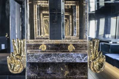 A grand, ornate fireplace with intricate gold-colored details and a dark, marble-like surface, set against a backdrop of wooden paneling and architectural elements.