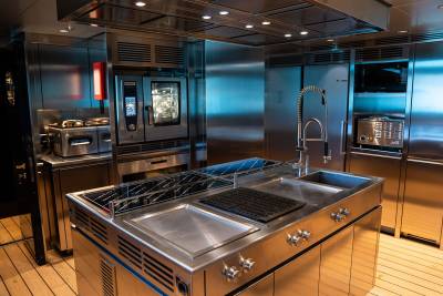 A modern, high-end kitchen with stainless steel appliances, a large cooktop, and a sleek, minimalist design featuring wooden floors and a tiled backsplash.