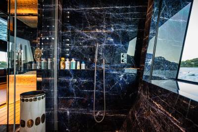 A luxurious bathroom with a glass wall overlooking a scenic landscape, featuring dark marble walls, a shower, and various toiletry items.