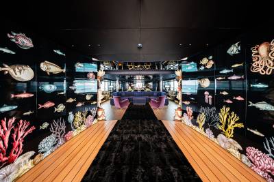 A vibrant underwater-themed restaurant interior with a wooden walkway, colorful coral and marine life displays on the walls, and a cozy seating area.