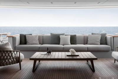 A cozy outdoor seating area with a large gray sofa, wooden coffee table, and wicker chairs overlooking the serene ocean in the background.