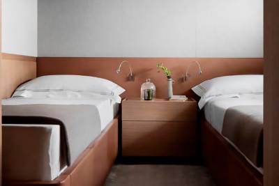 The image depicts a cozy bedroom with two twin beds, a nightstand between them, and various personal items such as a bottle and a plant on the nightstand.