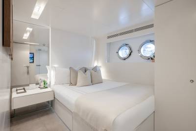 A bright and airy bedroom with a comfortable-looking bed, two circular windows, and a minimalist design aesthetic.