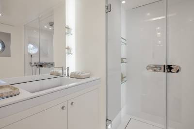 A modern, minimalist bathroom with a white vanity, a large mirror, and a glass-enclosed shower area.