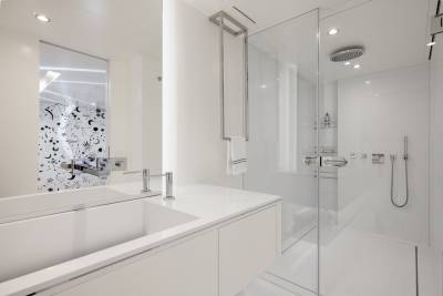 A modern, minimalist bathroom with a white vanity, a glass shower enclosure, and a patterned accent wall.
