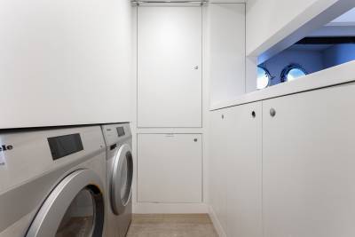 A modern, minimalist laundry room with a white washing machine and cabinets, set against a bright, clean background.