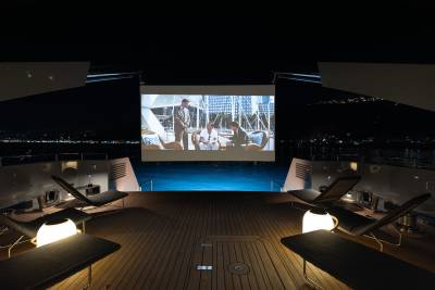 A luxurious outdoor cinema setup with comfortable lounge chairs, a large projection screen, and a scenic backdrop of a city skyline at night.