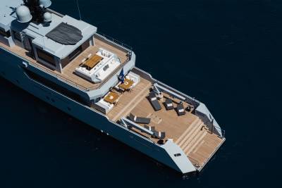 A large, luxurious yacht with a sleek, modern design sits on the dark waters, its deck and interior visible from an aerial perspective.