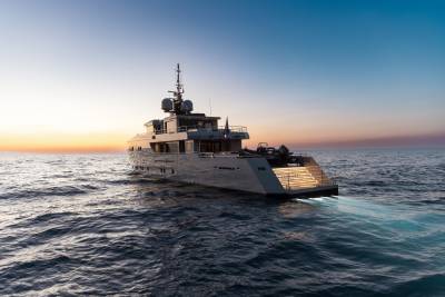 A large, luxurious yacht sailing on calm, turquoise waters against a backdrop of a vibrant sunset sky.