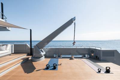 A modern yacht deck with a wooden floor, various exercise equipment, and a scenic view of the ocean in the background.