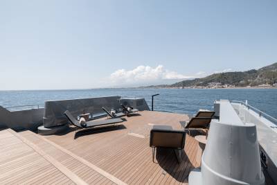 A wooden deck overlooking a scenic coastal landscape, with mountains and buildings in the background and a calm body of water in the foreground.