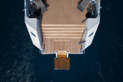 A large, luxurious yacht with a wooden deck and stairs extending over the dark blue water below.