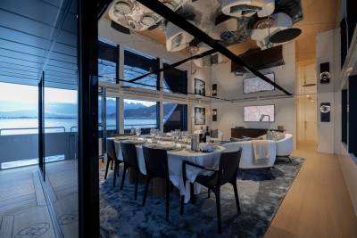 A modern and stylish dining room with a large table set for a meal, surrounded by comfortable chairs and featuring a stunning view of a body of water through the large windows in the background.