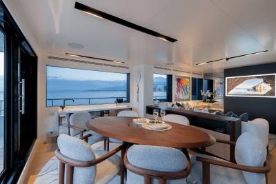A modern and stylish dining area with a large oval wooden table surrounded by comfortable chairs, overlooking a scenic body of water through the large windows in the background.