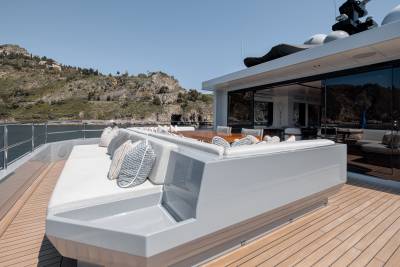 A modern, sleek yacht with a spacious deck overlooking a scenic mountainous landscape in the background.