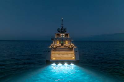 A large, illuminated yacht with a distinctive tower sits atop the calm, dark waters, surrounded by a serene, night-time landscape.