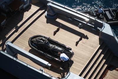 A wooden deck on a boat, with a golf bag and other equipment visible in the foreground, and the open water and sky in the background.