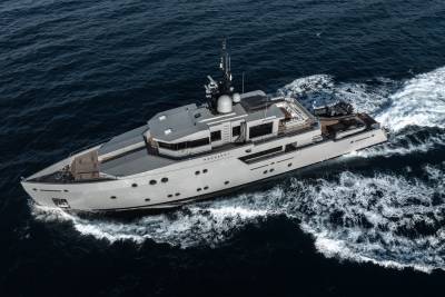 A large, gray yacht sailing across the deep blue ocean, leaving a trail of white waves in its wake.