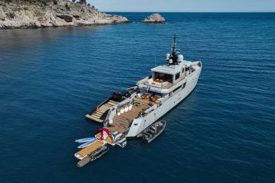 A large, luxurious yacht is anchored in a picturesque cove, surrounded by rugged cliffs and crystal-clear blue waters.