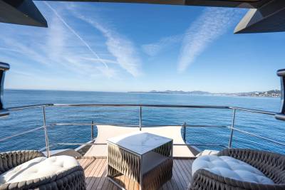 Two plush chairs and a modern table sit on a yacht's deck, overlooking a vast blue ocean under a clear sky with wispy clouds.
