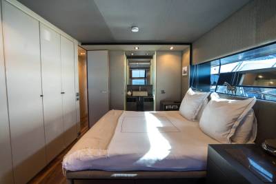 A neatly made bed with white linens and pillows dominates the foreground, while a well-lit bathroom with a sink and mirror is visible in the background.