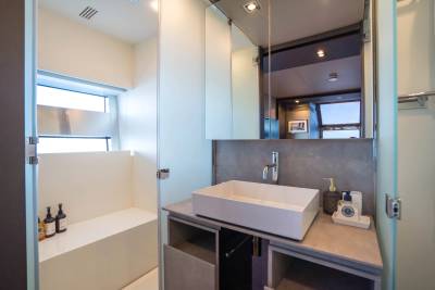 A modern bathroom with a white sink and vanity in the foreground and a shower stall with bottles in the background.