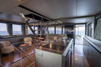 A modern yacht interior features a sleek kitchen island in the foreground and a living area with ocean views in the background.